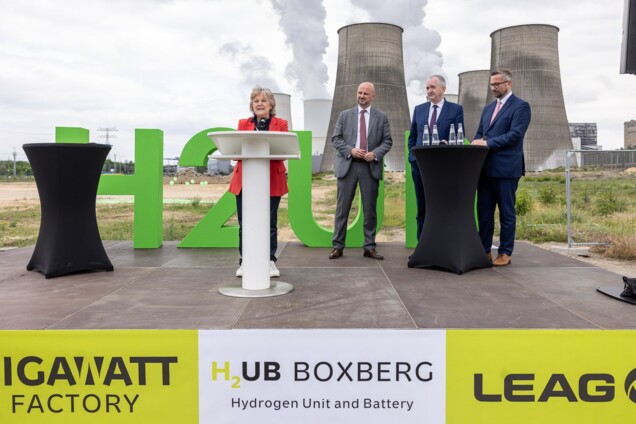 EU-Kommissarin Ferreira steht mit anderen Personen auf einer im Freien aufgebauten Bühne vor den Kühltürmen des Kraftwerks Boxdorf
