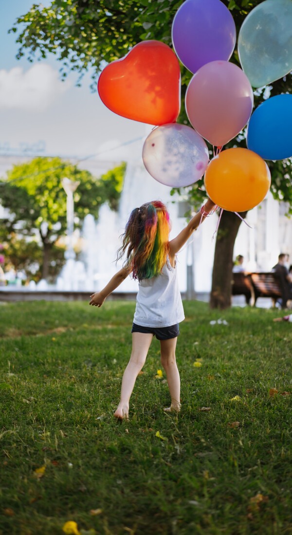 Ein Mädchen hält mehrere bunte Luftballons in der Hand